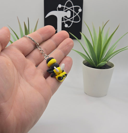 a hand holding a small articulated hornet on a keychain with plants and the crafticist logo in the background