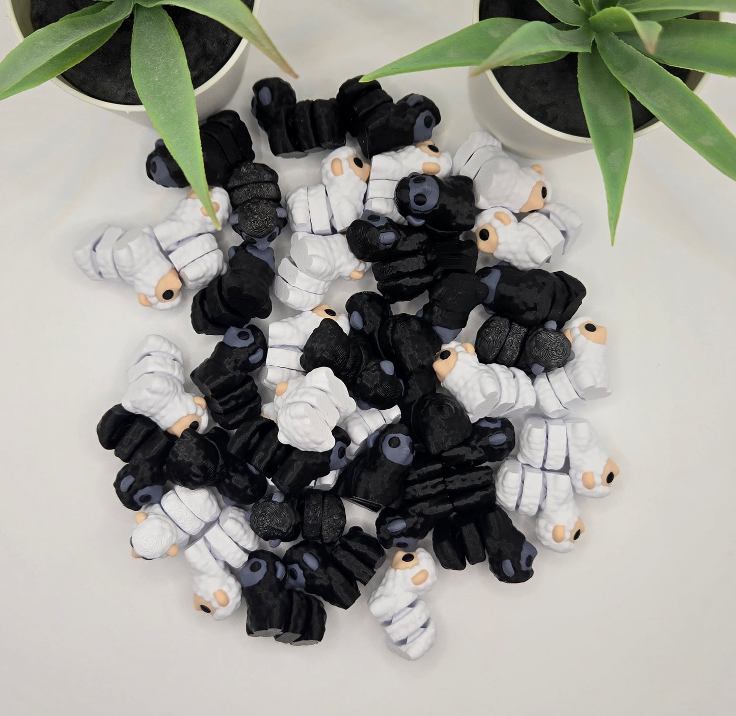 a pile of black and white articulated sheep toys on a white background with plants