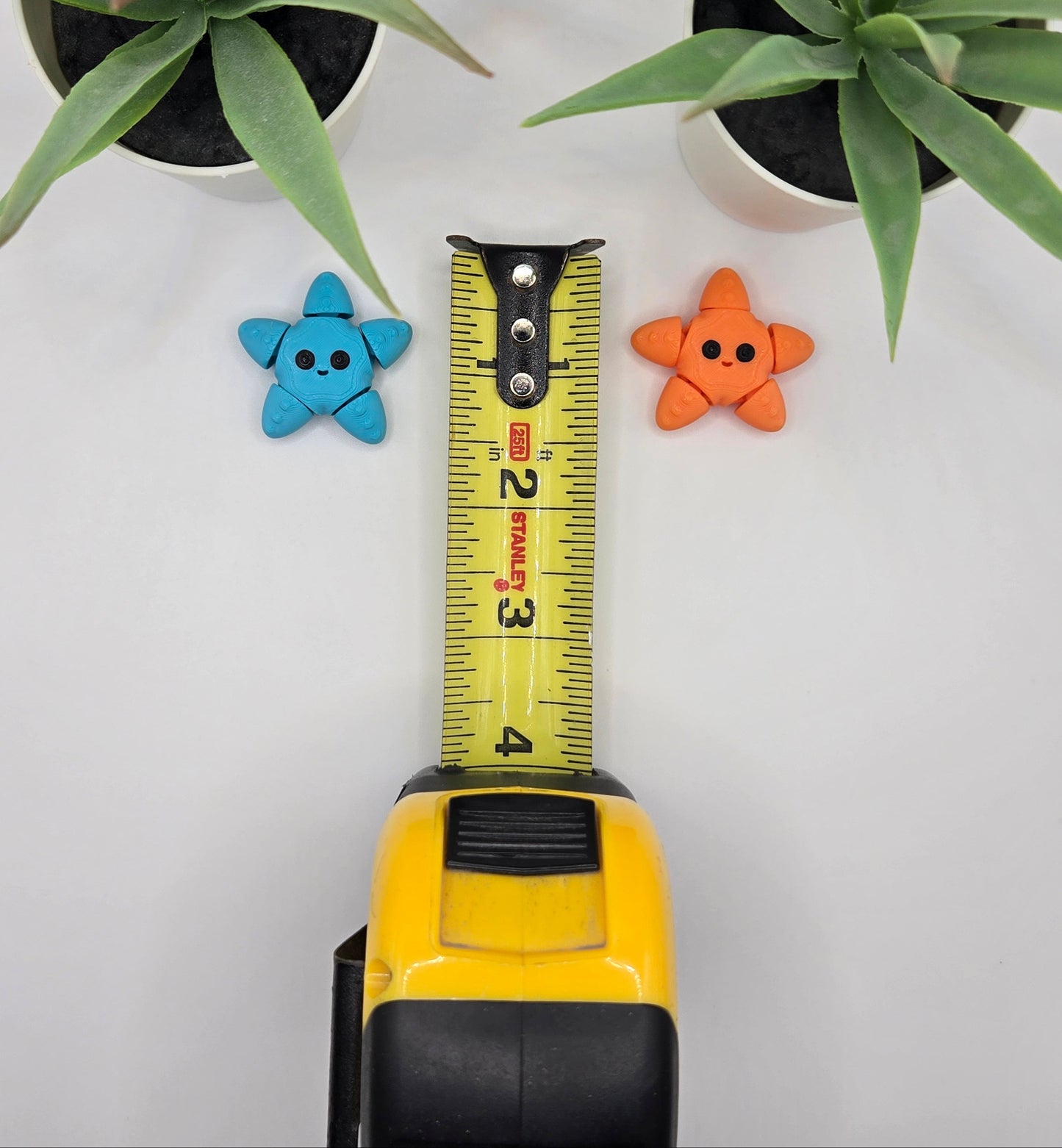 two articulated starfish toys with a tape measure on a white surface with plants in the background