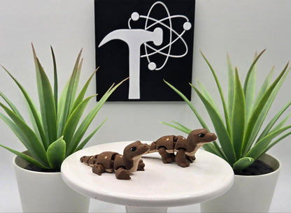 Two mini komodo dragon flexi animals on a white pedestal with plants and the Crafticist logo in the background.