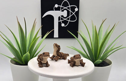 mini articulated komodo dragons on a white pedestal with plants and the Crafticist logo in the background