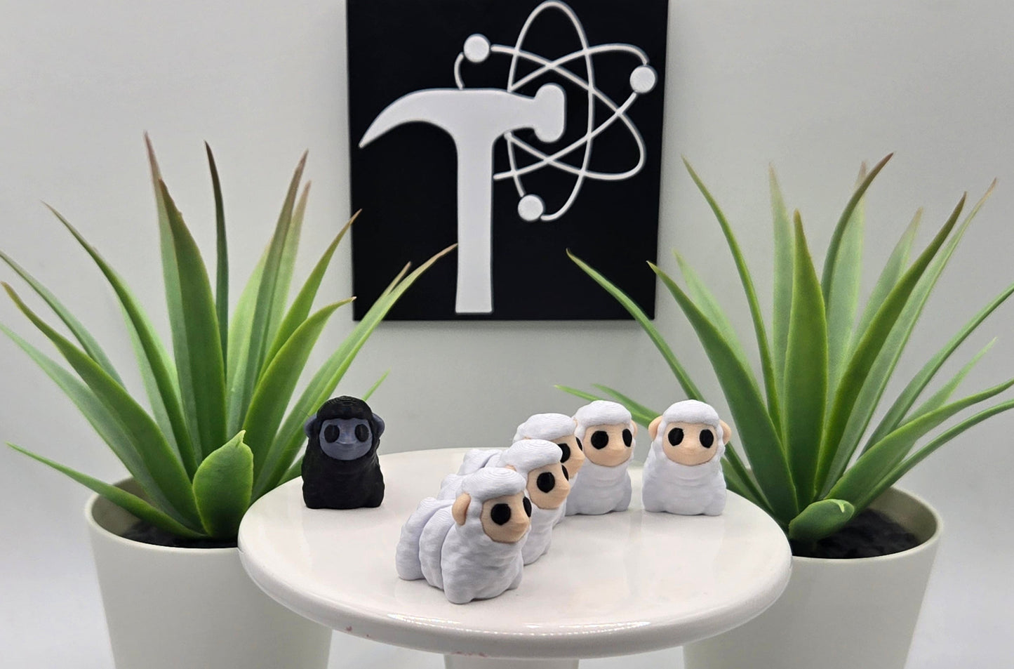 mini white and black articulated sheep on a white pedestal with two plants and the Crafticist logo in the background.