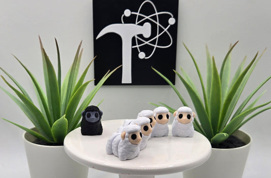 mini white and black articulated sheep on a white pedestal with two plants and the Crafticist logo in the background.