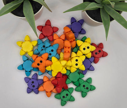 Colorful articulated starfish fidgets in a pile on a white background with two plants at the top.
