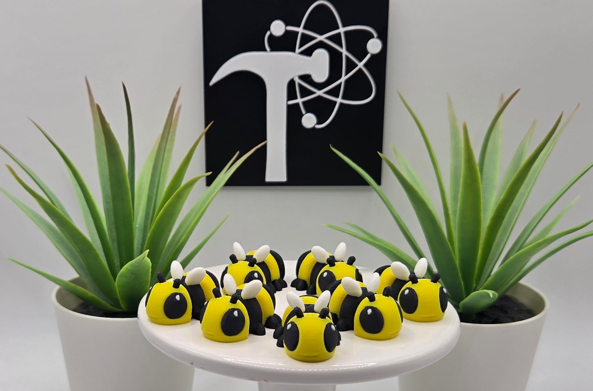 several mini articulated bees on a white pedestal with plants and the Crafticist logo in the background