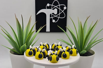 several mini articulated bees on a white pedestal with plants and the Crafticist logo in the background
