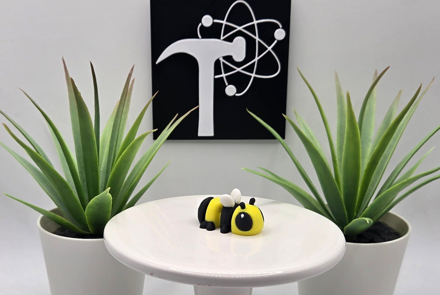 an articulated bumble bee toy on a white pedestal with plants and the Crafticist logo in the background