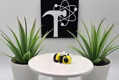 an articulated bumble bee toy on a white pedestal with plants and the Crafticist logo in the background