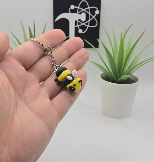hand holding an articulated bee keychain with plants and the crafticist logo in the background