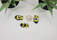 Three small bee toy figurines on a white surface with two potted plants in the background.
