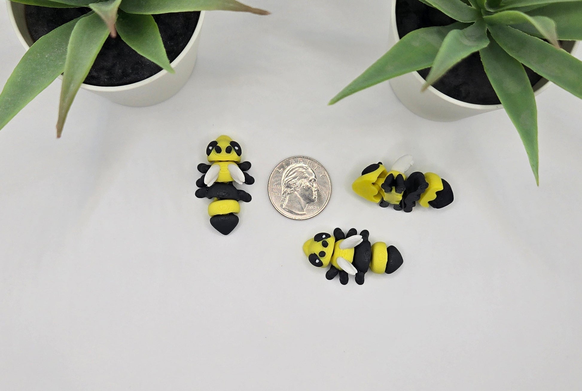 mini articulated hornet toys with a quarter on a white surface with plants