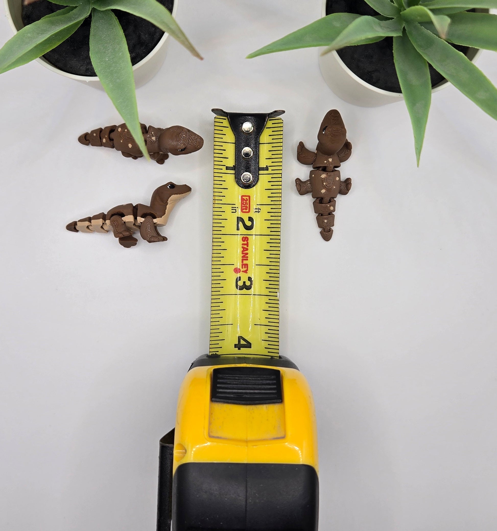 small articulated komodo dragon toys with a tape measure on a white surface with plants