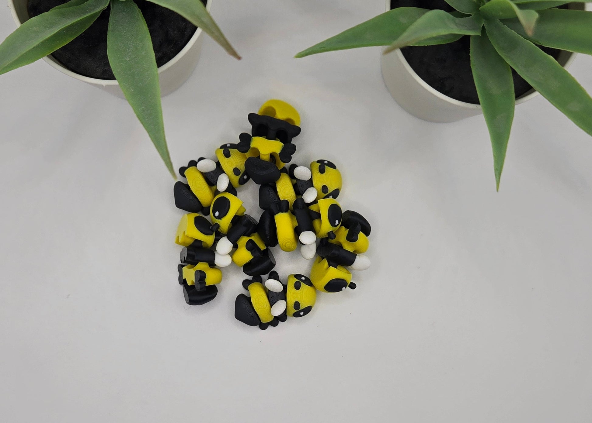 a pile of mini articulated bee toys on a white surface with plants in the background