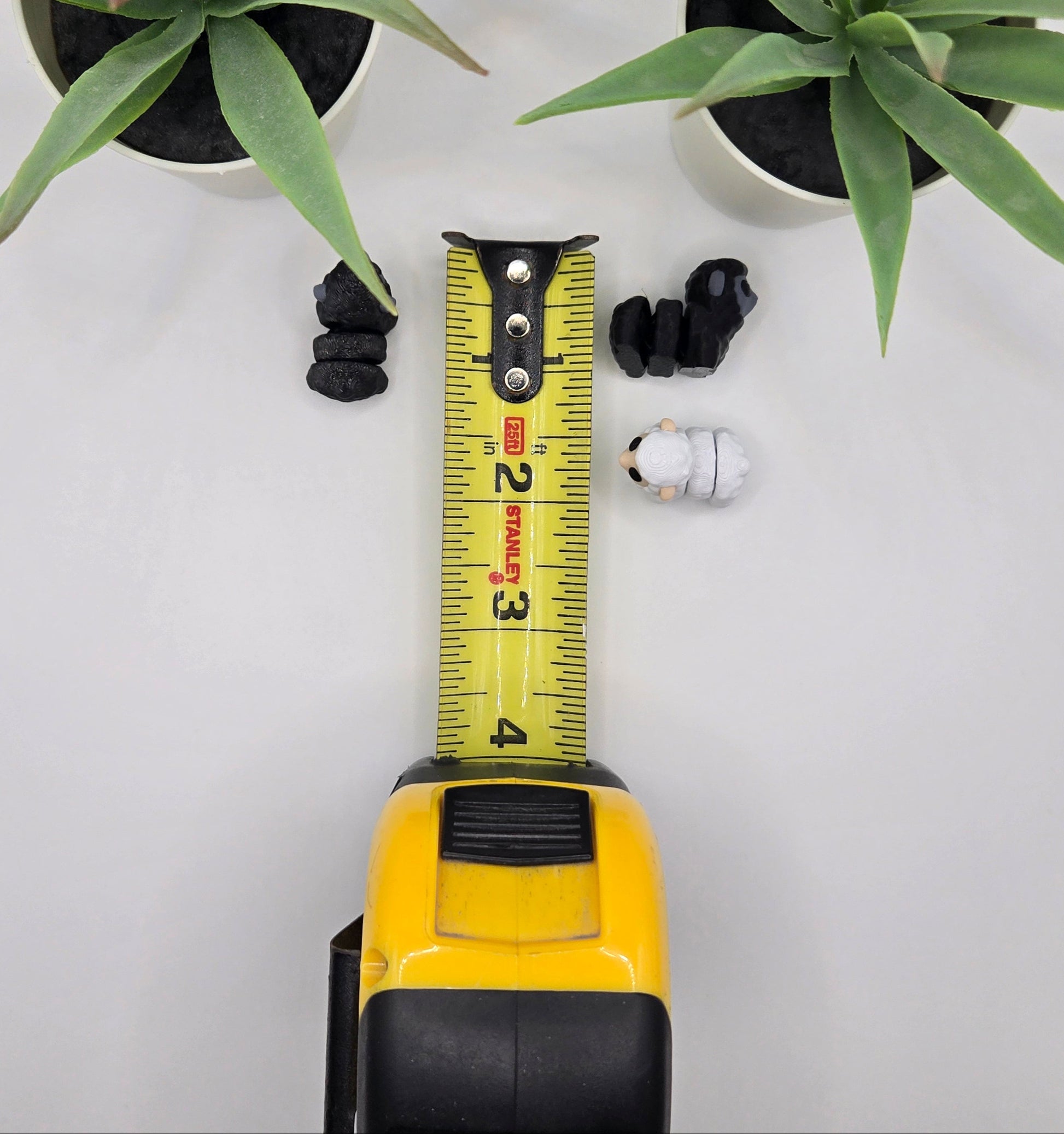black and white mini articulated sheep with a tape measure on a white background with plants
