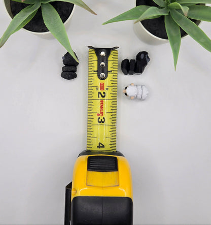 black and white mini articulated sheep with a tape measure on a white background with plants