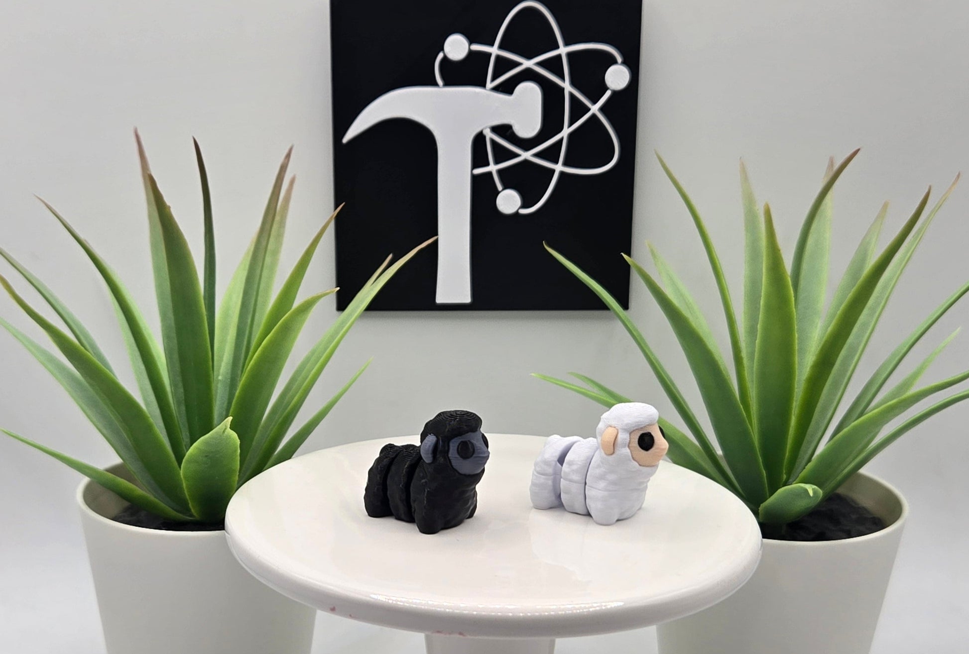 black and white articulated sheep on a white pedestal with plants and the crafticist logo in the background